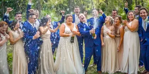 A bride and groom celebrating with their wedding party outdoors, spraying champagne.