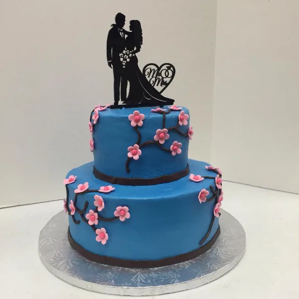 A two-tiered blue wedding cake decorated with pink sugar flowers and a black Mr and Mrs silhouette topper.
