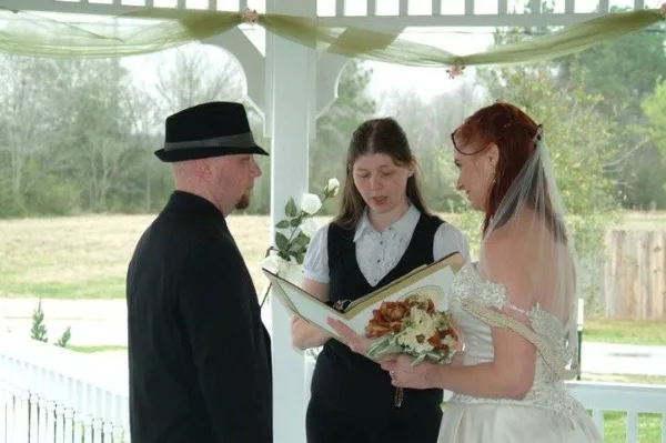 A woman officiating a wedding ceremony for a bride and groom in a white gazebo.