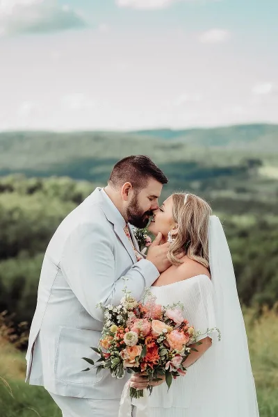 A bride and groom sharing a kiss outdoors with a scenic landscape background.