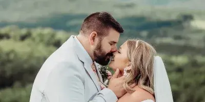 A bride and groom sharing a kiss outdoors with a scenic landscape background.