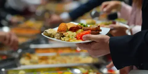 A server holding a plate of assorted food items in front of a buffet line at an event.