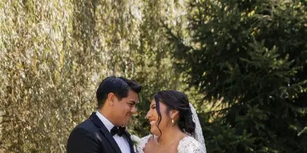 A bride and groom standing outdoors, with the bride holding a large white floral bouquet.