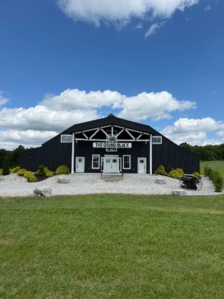 Exterior view of a large black barn event venue with white trim and a sign reading 'The Grand Black'.