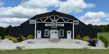 Exterior view of a large black barn event venue with white trim and a sign reading 'The Grand Black'.