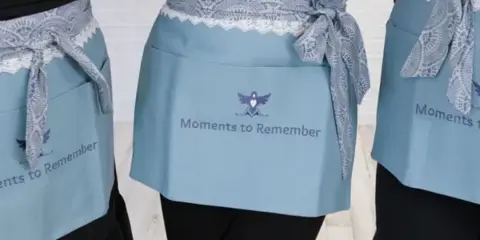 Close-up of light blue aprons with lace trim, featuring the 'Moments to Remember' logo and name.