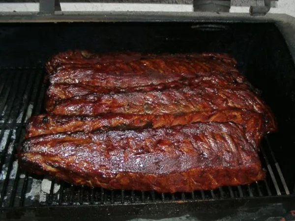 A rack of BBQ ribs cooking on a grill grate.