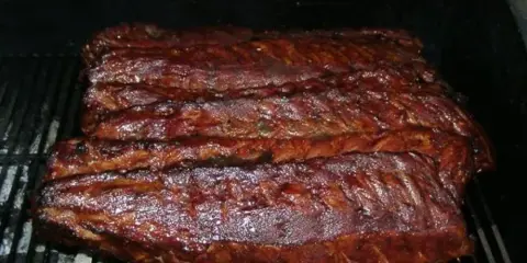 A rack of BBQ ribs cooking on a grill grate.