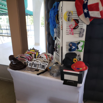 A photo booth station set up with a camera and a rack of party props including hats and glasses.