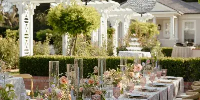 Outdoor wedding reception table set with floral arrangements, glassware, and hanging crystal orbs under a leafy canopy.