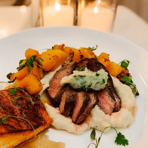Plated dish of sliced roast beef over mashed potatoes with roasted potatoes and herb garnish on a white plate.
