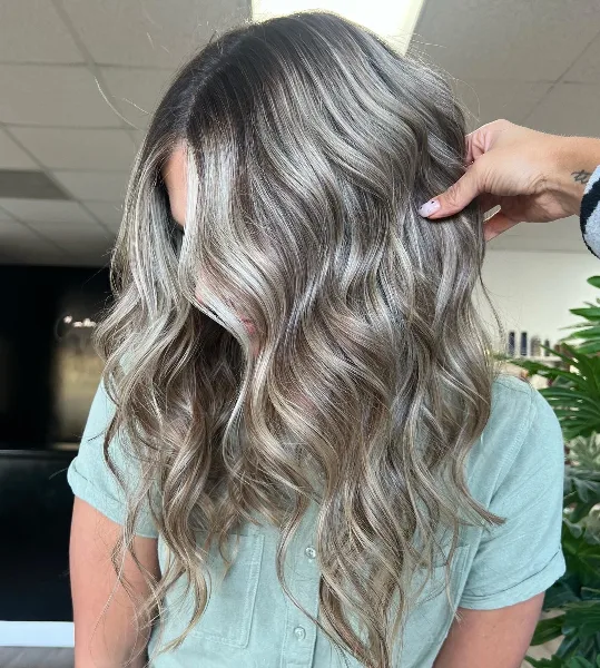 Close-up of a client's wavy, highlighted hair being styled by a professional.