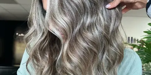 Close-up of a client's wavy, highlighted hair being styled by a professional.