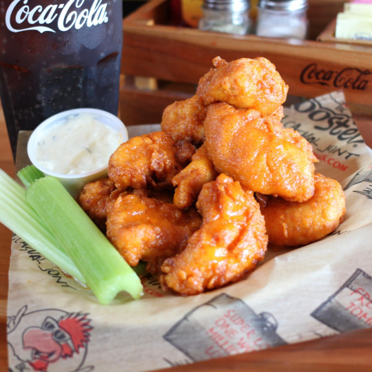 A basket of fried chicken wings served with celery and a dipping sauce.