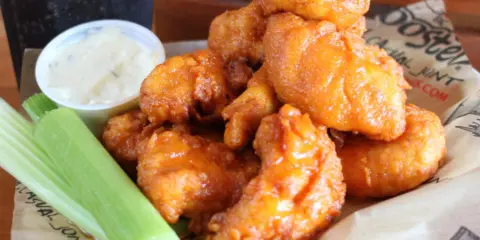 A basket of fried chicken wings served with celery and a dipping sauce.