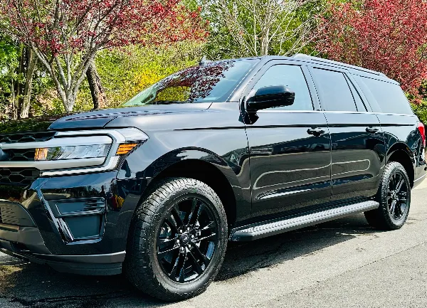 A black SUV parked on a paved surface with trees in the background.