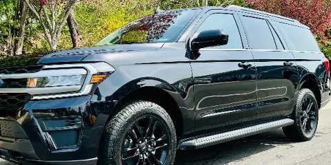 A black SUV parked on a paved surface with trees in the background.