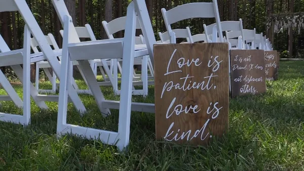 White folding chairs arranged on a grassy lawn with wooden signs reading 'Love is patient, love is kind'.
