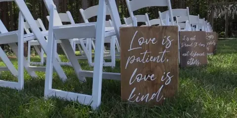 White folding chairs arranged on a grassy lawn with wooden signs reading 'Love is patient, love is kind'.