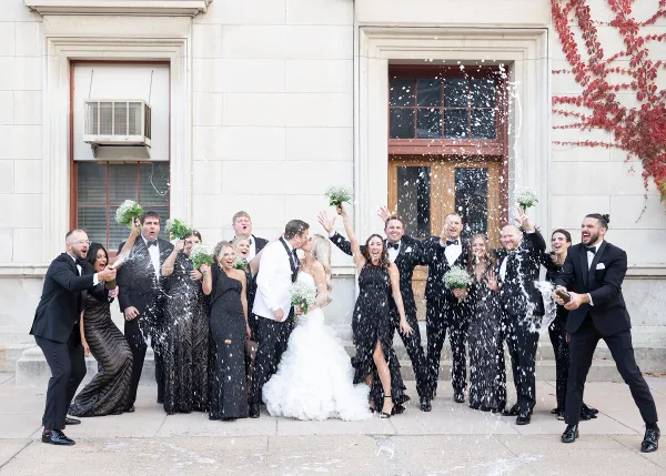 A wedding party celebrating with champagne and confetti in front of a stone building.
