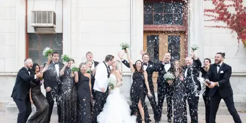A wedding party celebrating with champagne and confetti in front of a stone building.