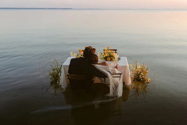 A bride and groom seated at a table in the water during a destination wedding.