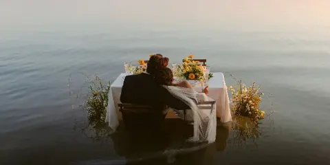 A bride and groom seated at a table in the water during a destination wedding.