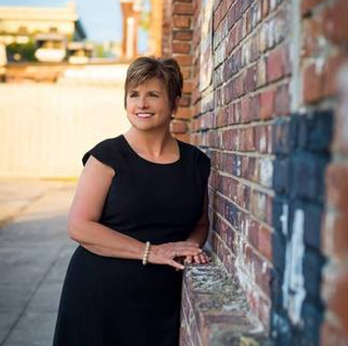 Portrait of Donna Brown, a woman in a black dress, standing against a brick wall.
