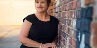 Portrait of Donna Brown, a woman in a black dress, standing against a brick wall.