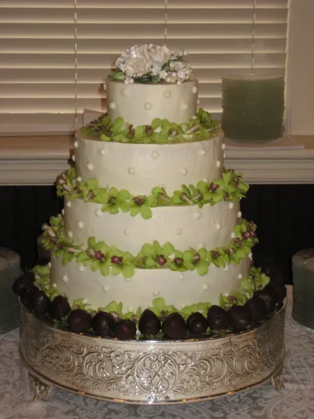 A four-tier white wedding cake decorated with green flowers and chocolate truffles on a silver stand.