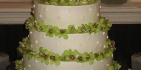 A four-tier white wedding cake decorated with green flowers and chocolate truffles on a silver stand.