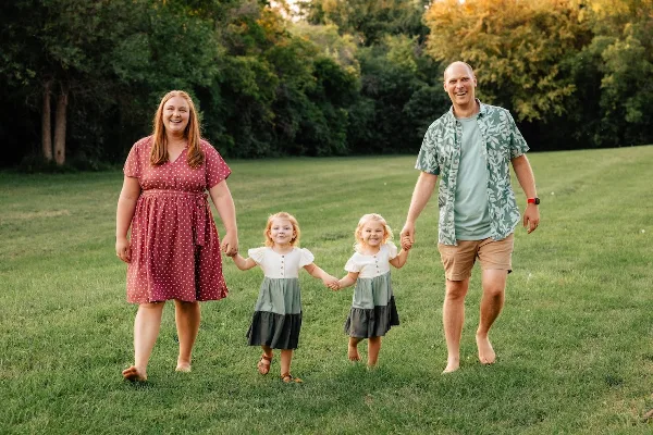 A family of four standing on a grassy field holding hands, captured in a professional outdoor portrait.