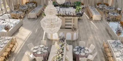 Interior view of a clear-top event tent featuring chandeliers, lounge seating, and multiple dining tables set with tableware.