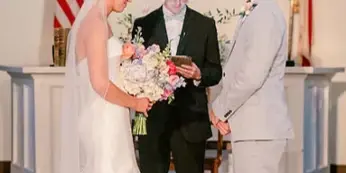 A bride and groom exchanging vows with an officiant in a historic courtroom setting.