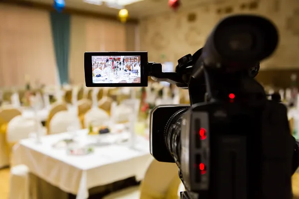 A professional video camera with an active LCD screen recording a wedding reception in a banquet hall.
