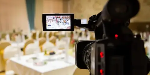 A professional video camera with an active LCD screen recording a wedding reception in a banquet hall.