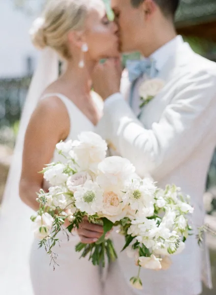A bride and groom sharing a kiss while the bride holds a white floral bouquet.