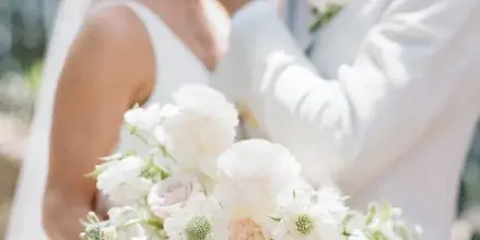 A bride and groom sharing a kiss while the bride holds a white floral bouquet.