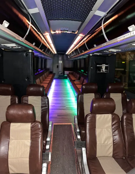 Interior of a party bus with brown leather seats and colorful LED lighting along the aisle.