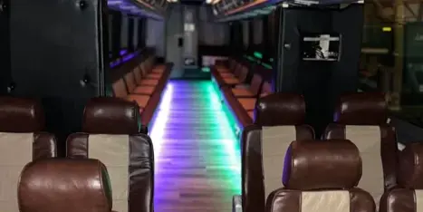 Interior of a party bus with brown leather seats and colorful LED lighting along the aisle.