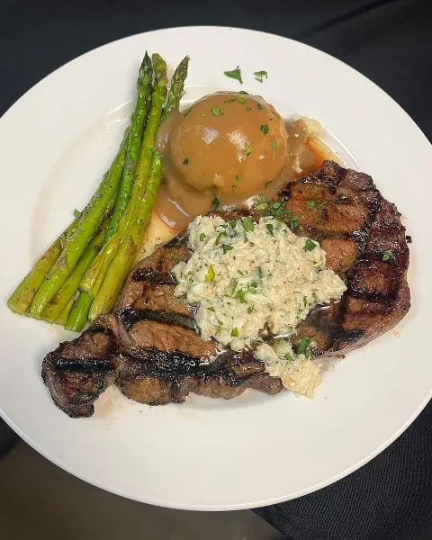 A grilled steak on a white plate with asparagus, mashed potatoes, and gravy