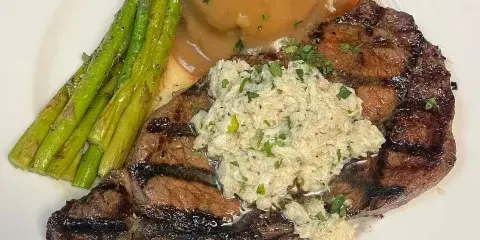 A grilled steak on a white plate with asparagus, mashed potatoes, and gravy