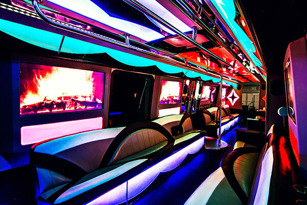 Interior view of a party bus featuring curved seating, colorful LED lighting, and large windows.