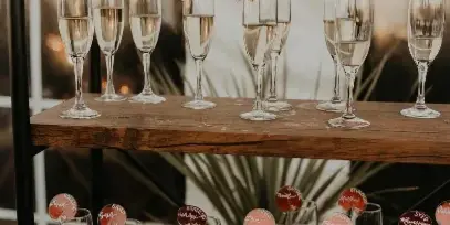A wooden serving cart holding rows of champagne flutes with personalized name tags, set against a white backdrop.