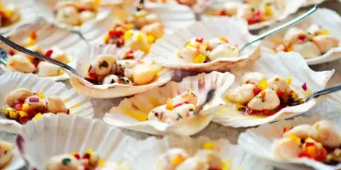 A close-up photograph of scallops topped with a colorful vegetable salsa, served in their shells.