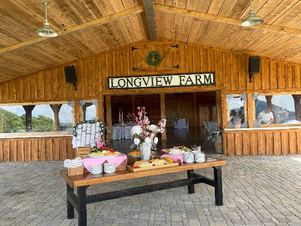 Exterior view of Longview Farm event venue featuring a wooden facade, outdoor patio, and a catering table with food and floral arrangements.
