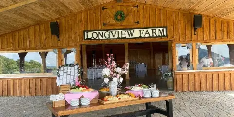 Exterior view of Longview Farm event venue featuring a wooden facade, outdoor patio, and a catering table with food and floral arrangements.