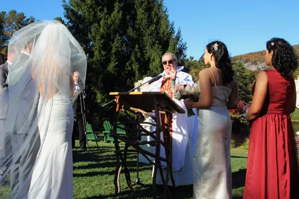 An Orthodox Catholic priest officiating an outdoor wedding ceremony for a bride and groom.