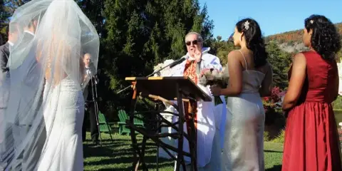An Orthodox Catholic priest officiating an outdoor wedding ceremony for a bride and groom.