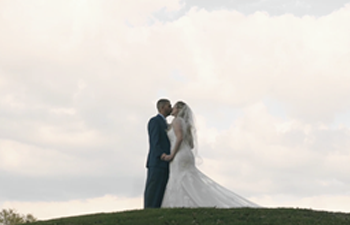 Bride and groom embracing on a grassy hill under an overcast sky